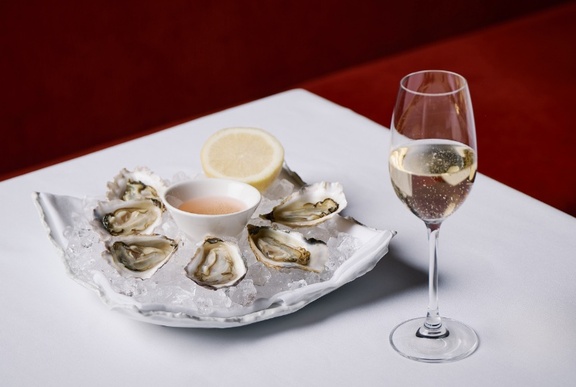 Tray of oysters with lemon next to a glass of champagne on a white-linen table.