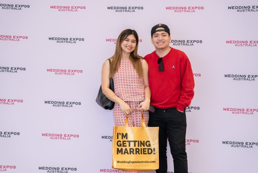 Two people smiling while holding an I'm Getting Married bag. 
