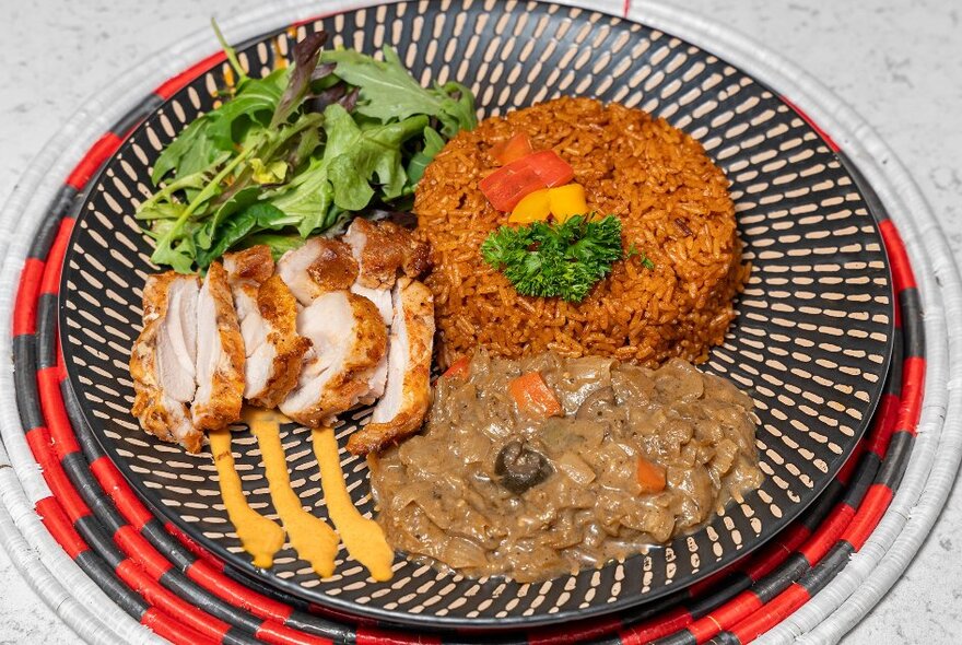 Dish of African food including sliced meat, rice and stew on a plate with black geometric pattern.