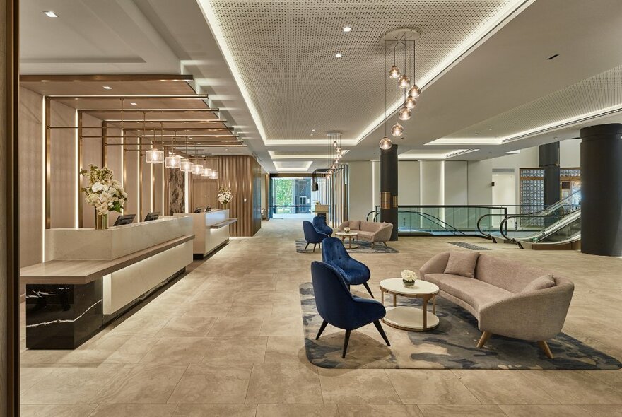 A vast, empty hotel lobby space with beige tones and two blue chairs. 