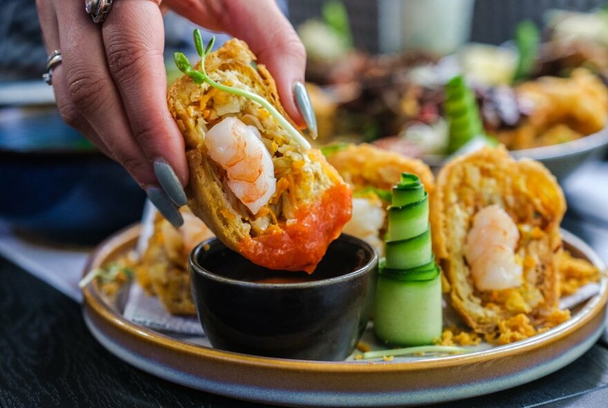 A hand dipping a filled pastry into a dipping sauce.