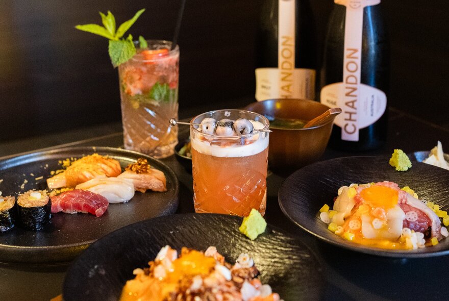 Tropical cocktails and champagne with black bowls of Asian food.