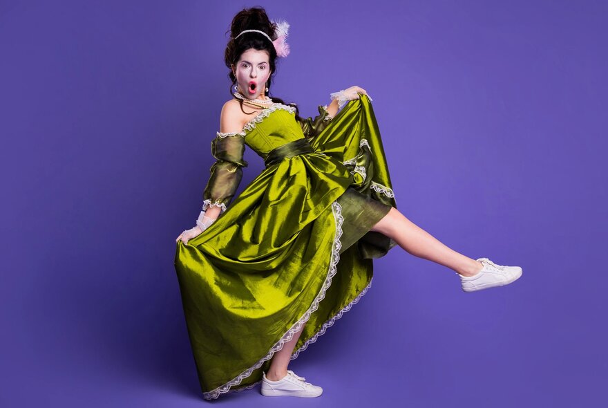 A person modeling a bright green, historical-style dress paired with modern white sneakers against a purple background.