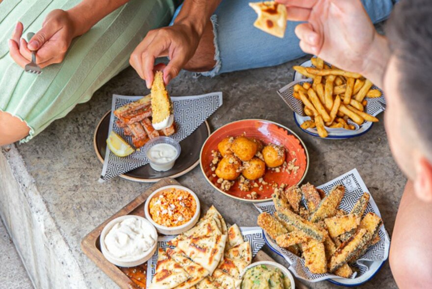 Bird's-eye of selection of dishes on stone bench,  small bits of people visible, grabbing food.