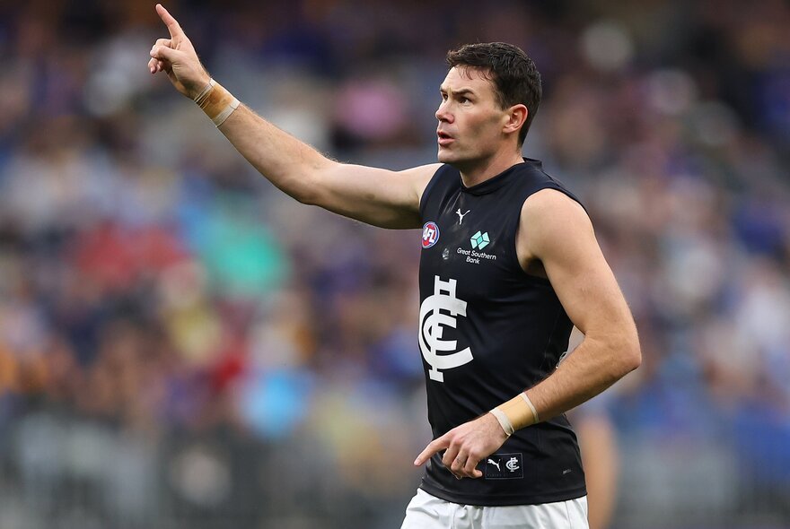 A Carlton AFL player with his arm raised on a football field.