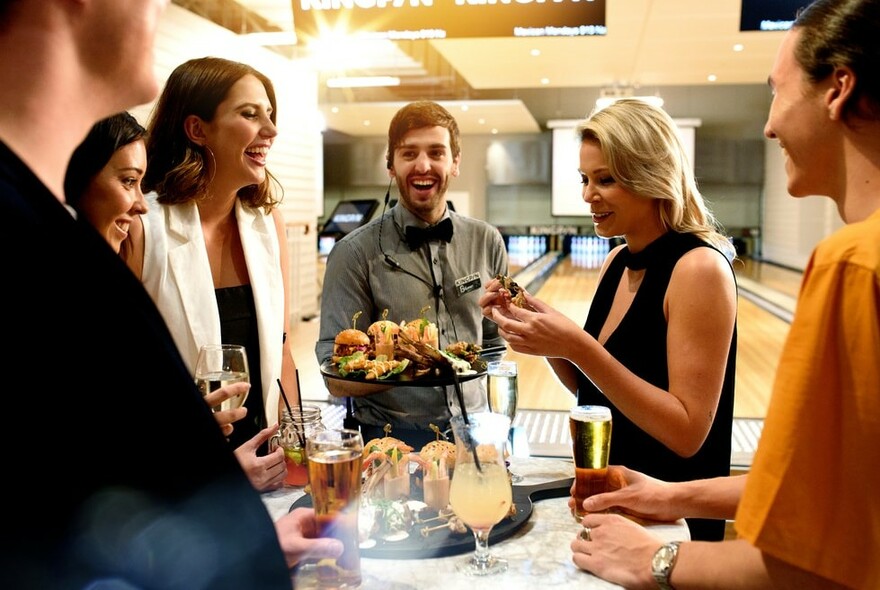 People enjoying drinks and burgers at a bowling alley.