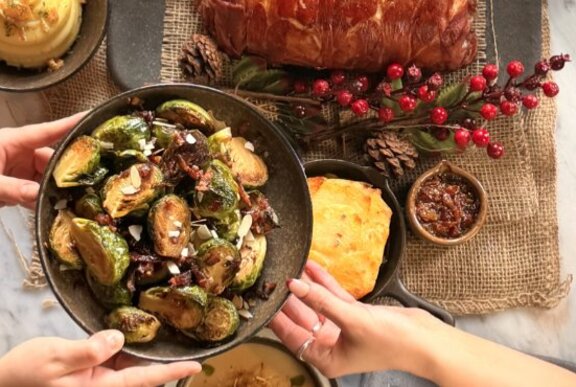 Christmas roast dinner feast of pork and brussels sprouts with hands reaching for plate.