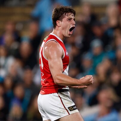 A St Kilda AFL football player with his fists clenched and pumped during a match, a blurred stadium crowd in the background.