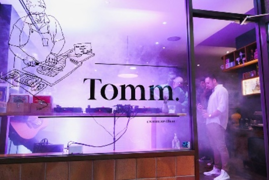 The exterior of Tomm's wine bar with people standing inside and signage on the window. 