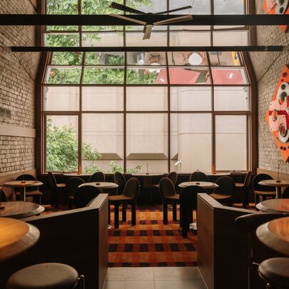 Brick-lined wine bar with round tables and seating, with wall of windows opening onto a courtyard.