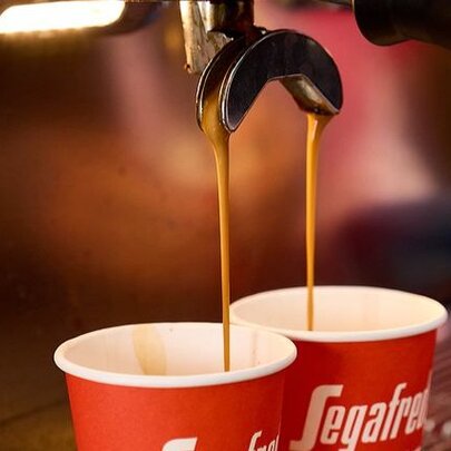 Fresh espresso coffee being poured from an espresso machine into red takeaway cups.