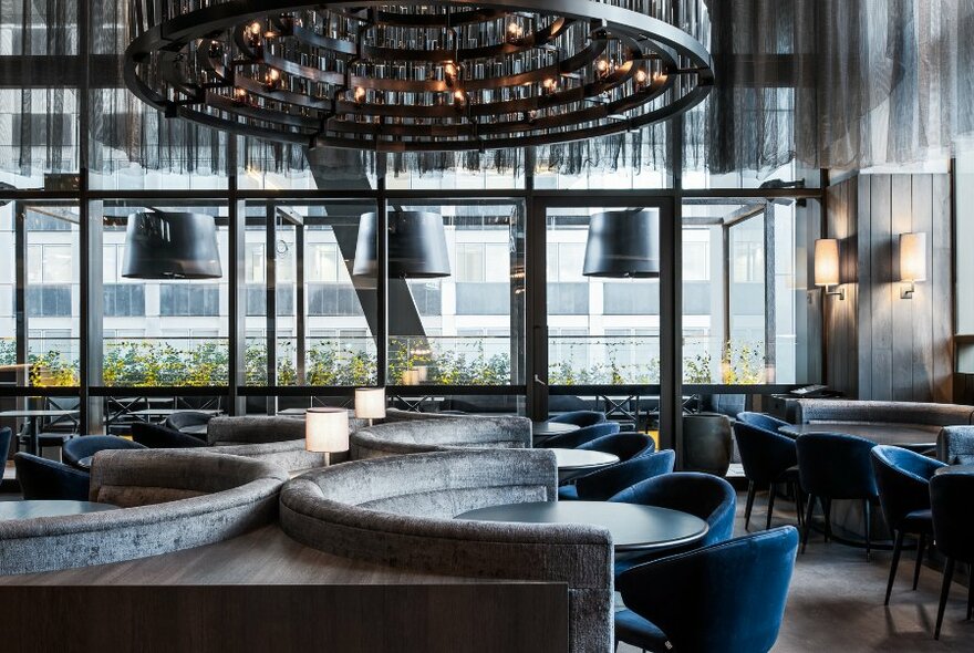 A dining space with large windows and blue velvet seating. 