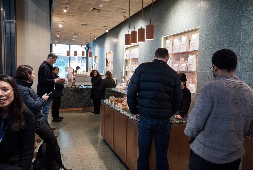 Customers in a green-tiled cafe milling about, waiting for their coffees or waiting to order.