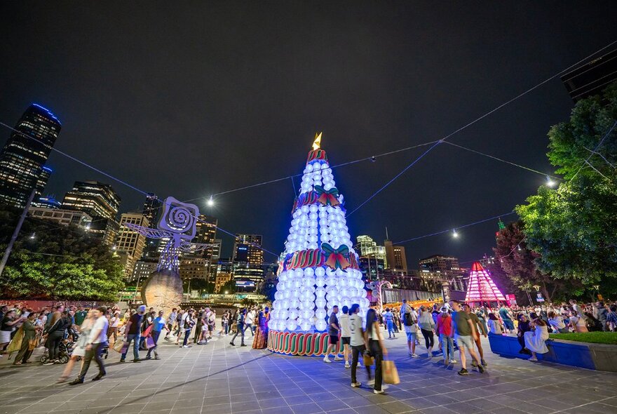 People standing around giant Christmas decorations with koalas climbing lit-up candy canes at Queensbridge Square at night, city buildings in the background.