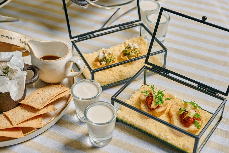 Two open glass presentation cases with a selection of sweet and savoury cheese treats in them, alongside two small glasses of milk and a cheese platter.