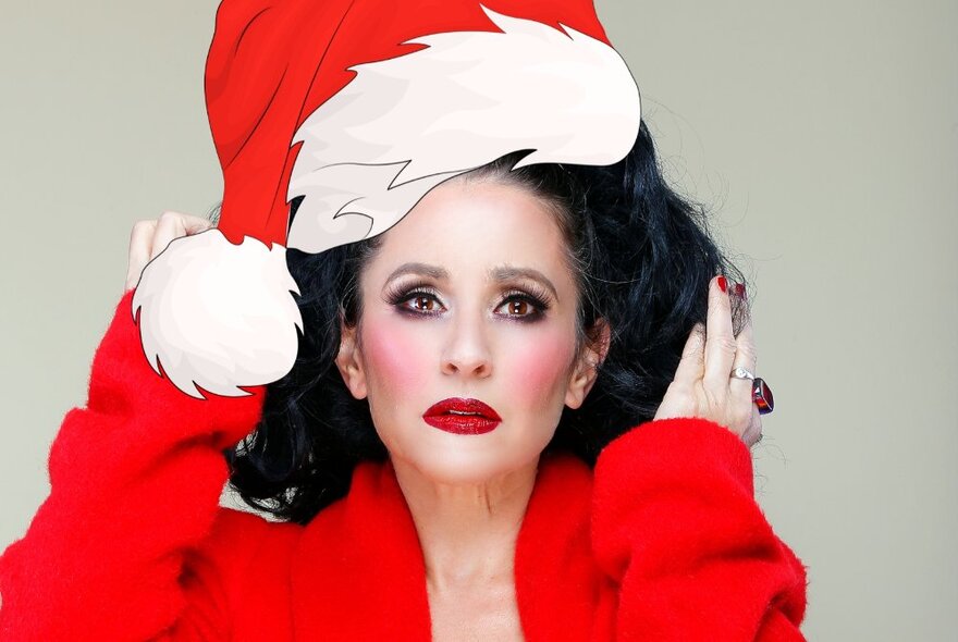 Performer Lucy Best wearing an oversized red jacket and a red santa cap; dark red lipstick and looking directly at the viewer.