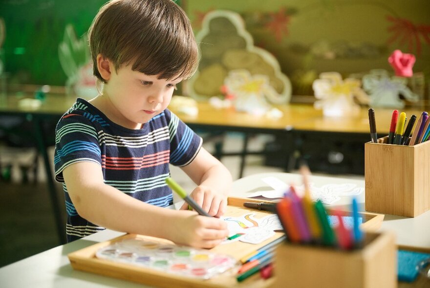 A child drawing at a table set up for craft. 