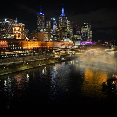 Melbourne city skyline illuminated at night, viewed across the Yarra River, with a bridge in the middle-ground shrouded in mist.