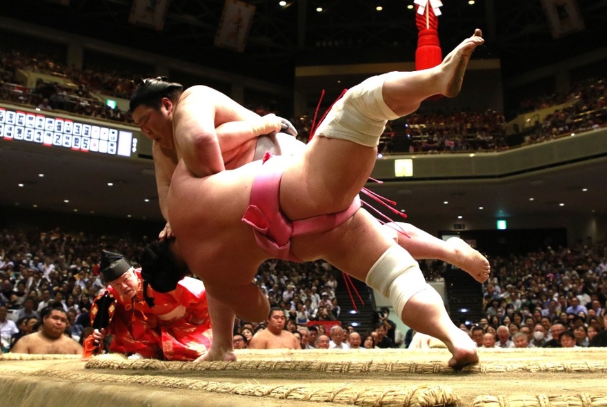 Sumo wrestlers hurling each other to the ground during a tournament in Japan.