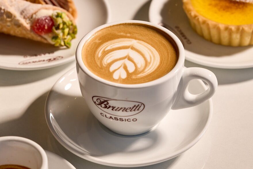 A close up of a Brunetti Classico flat white with pastries in the background. 