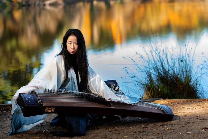 Mindy Meng Wang playing the guzheng by the side of a lake.