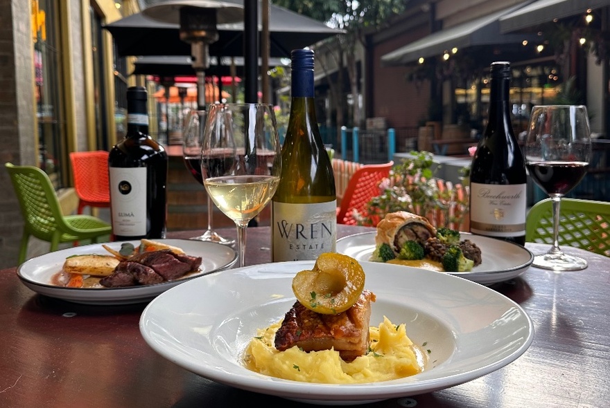 A table setting in a wine bar with plates of food, wine glasses and bottles.