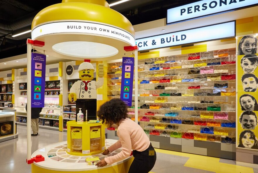 A person using the build-your-own Lego person wall inside a shop.