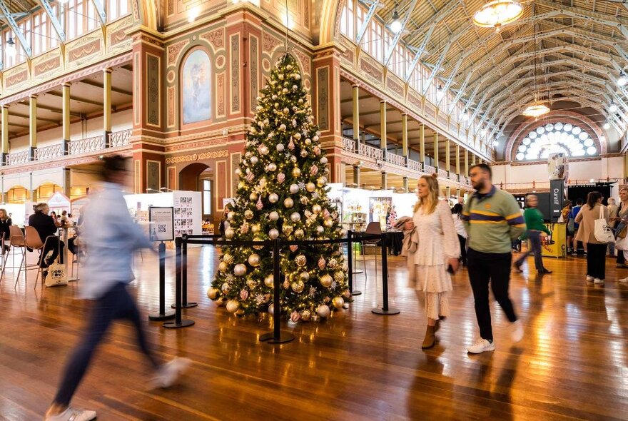 People walking past a Christmas tree with gold baubles in the Exhibition Building.