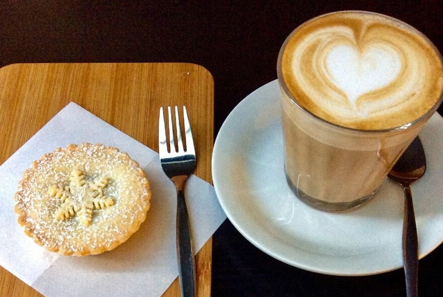 Small tart next to a cafe latte.