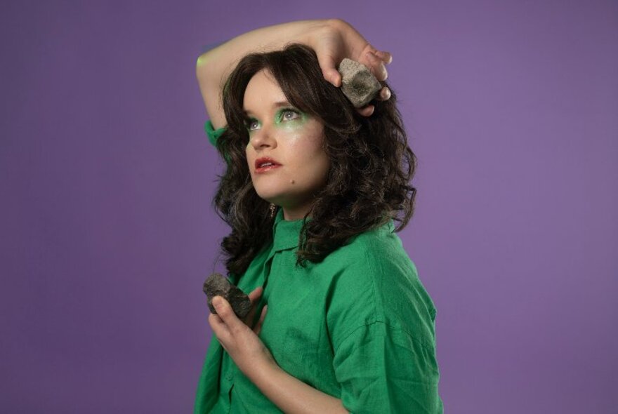 Comedian wearing green eye makeup and shirt, holding rocks in her hands.