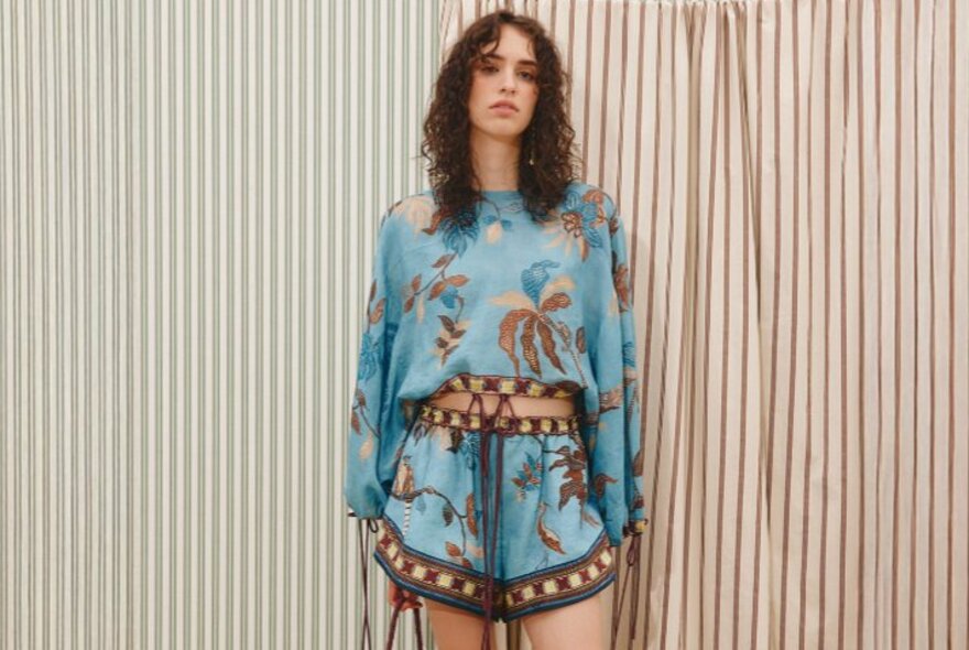 A model wearing a matching blue crop top and shorts with a burgundy leaf print.