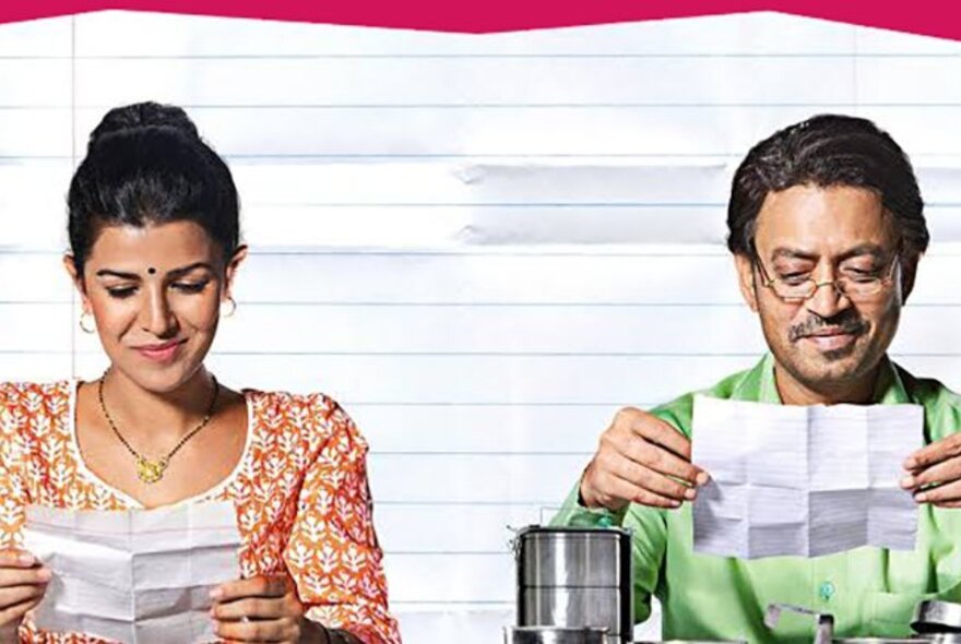 Indian man and woman seated reading folded sheets of white paper.