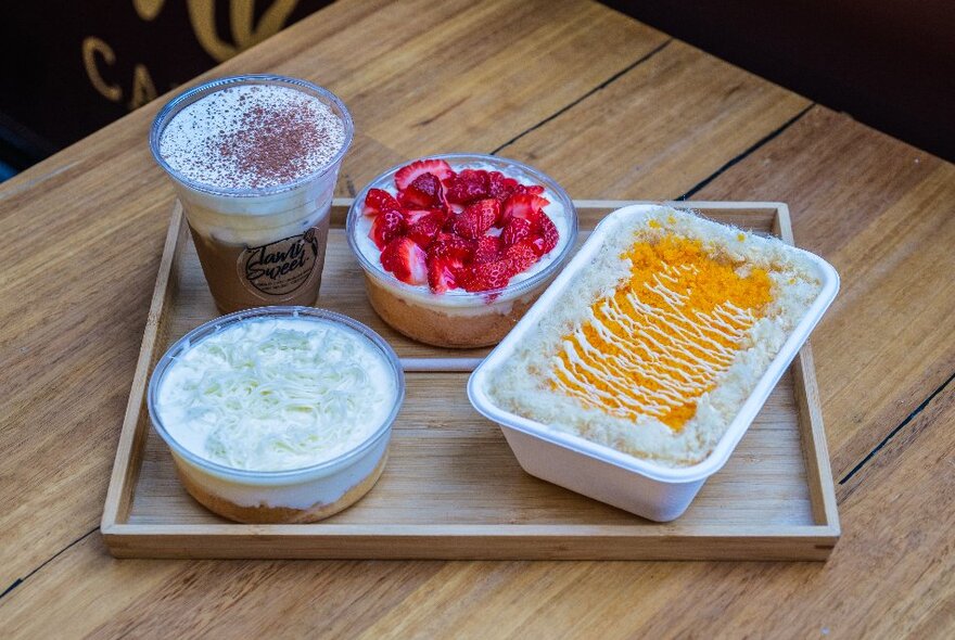 A bamboo tray of creamy desserts with fruit on top and an iced coffee with cream.