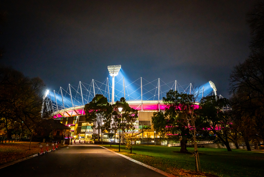 MCG football stadium lit up pink at night.