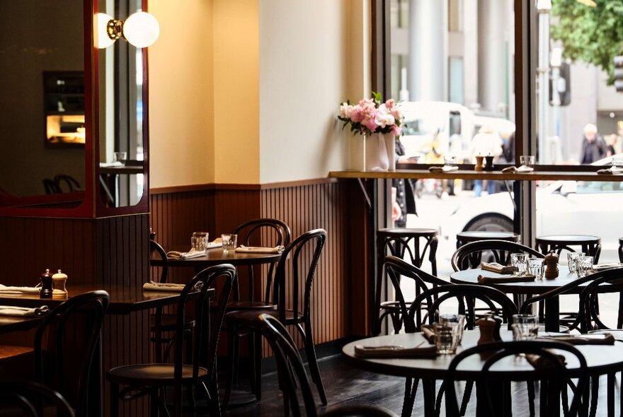 Bistro tables and chairs in a cafe set for dining in front of large windows.