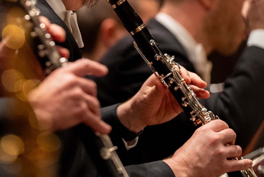 Close up of people playing the oboe in an orchestra setting. 
