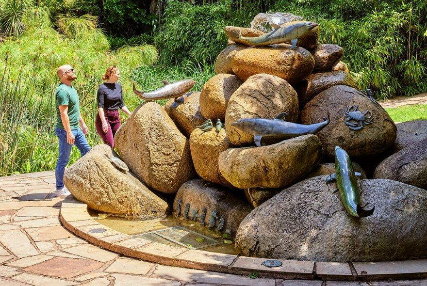 Two people standing next to the Dolphin Fountain in Fitzroy Gardens. 