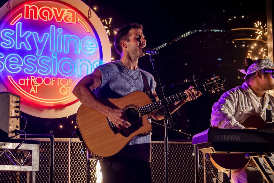 A guitarist singing on stage in front of a round illuminated sign that says Skyline Sessions. 