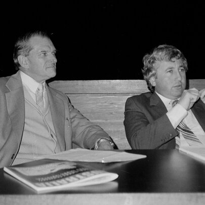 Black and white picture of two labour politicians, Bill Kelty and Laurie Carmichael, seated at a conference table.