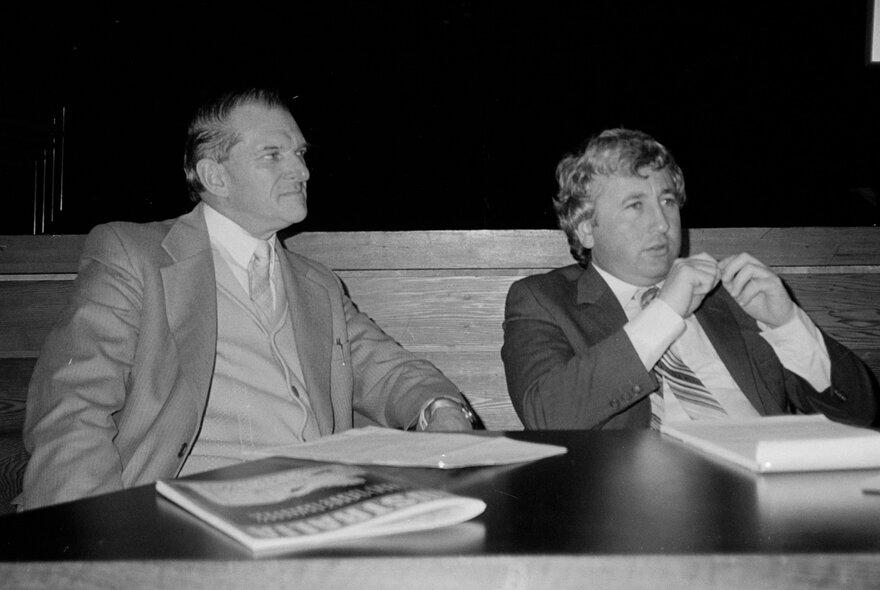 Black and white picture of two labour politicians, Bill Kelty and Laurie Carmichael, seated at a conference table.