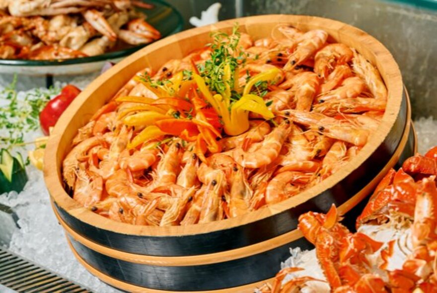 A large wooden platter filled to the brim with cooked prawns in their shells.