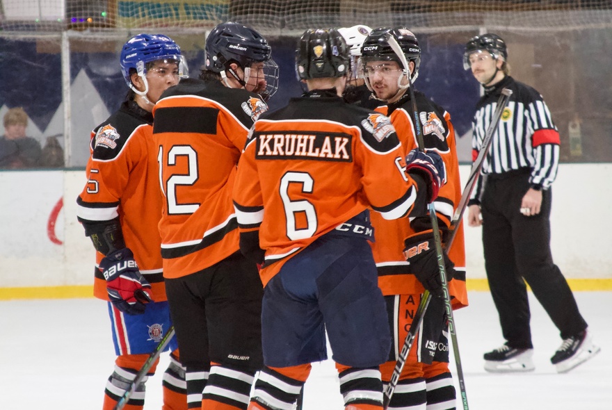 Players from the Melbourne Mustangs ice hockey team wearing their orange and black jerseys during an ice hockey league match on an ice rink.