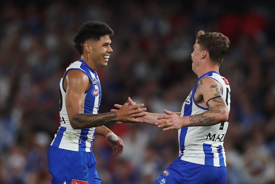 Two North Melbourne players slap hands on the field looking happy. 