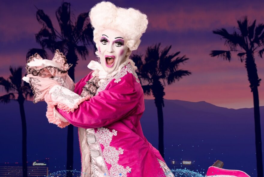 Cabaret performer dressed in pink Louis XV court dress and white wig with white make-up and mouth wide open.