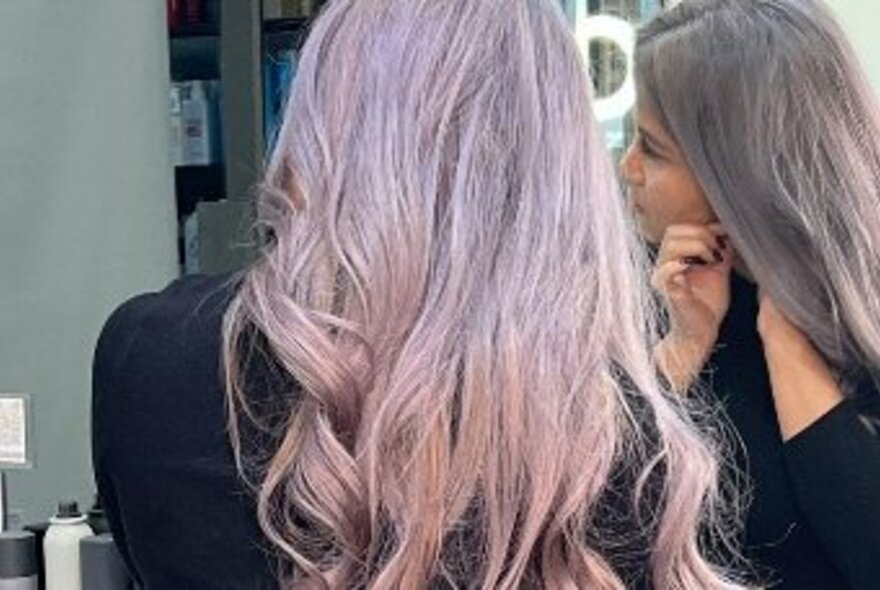 Woman with long purple hair putting on earrings.