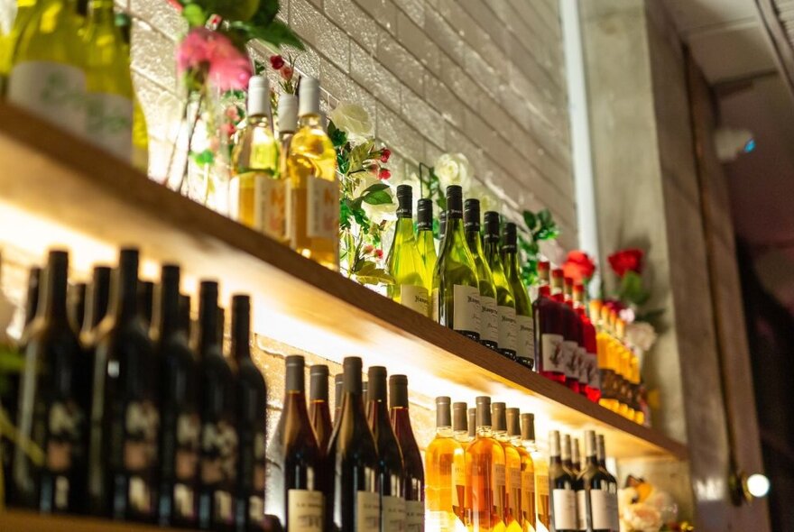 Interior of a restaurant with bottles  of wine lined up on a shelf against a wall.