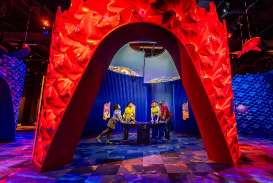 Inside Melbourne Museum's Our Wondrous Planet exhibition showing people gathered around a display through a red fiery archway.