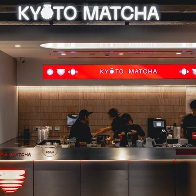 The counter of Kyoto Matcha with the name in neon over a workspace where staff are preparing drinks. 