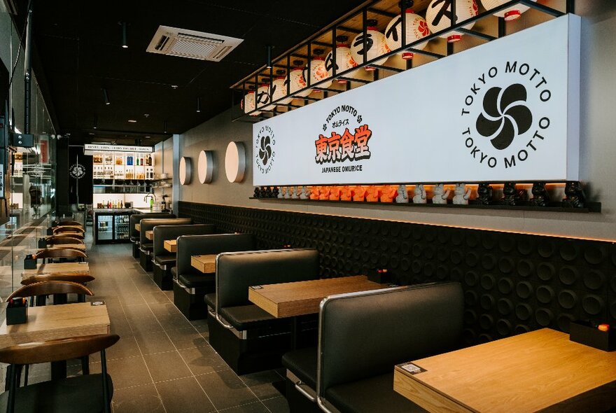 Interior of Tokyo Motto restaurant showing booth seating along one wall and small table for two along the other wall, a kitchen at the rear.