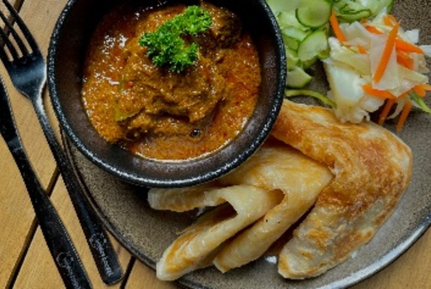 Bowl of curry with roti and salad alongside.